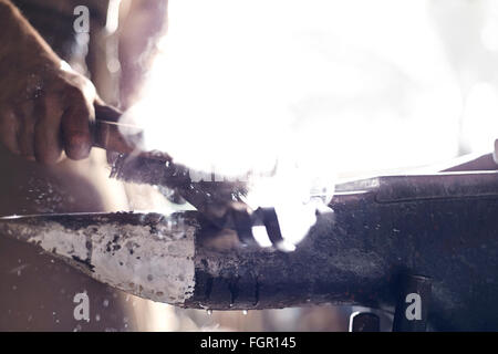 Close up of blacksmith brushing iron tool over anvil in forge Stock Photo