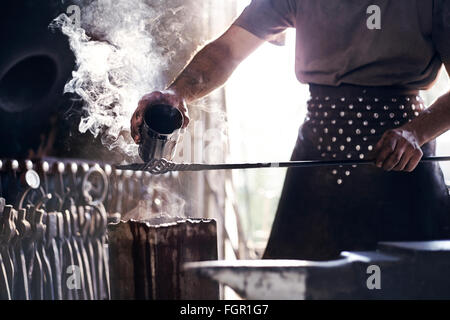 Blacksmith pouring hot liquid over wrought iron in forge Stock Photo