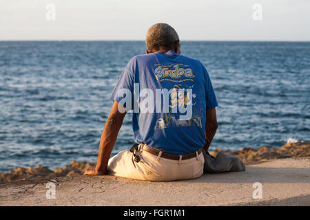 Daily life in Cuba - Local Cuban man sitting on wall looking out to sea at El Malecon, Havana, Cuba, West Indies, Caribbean