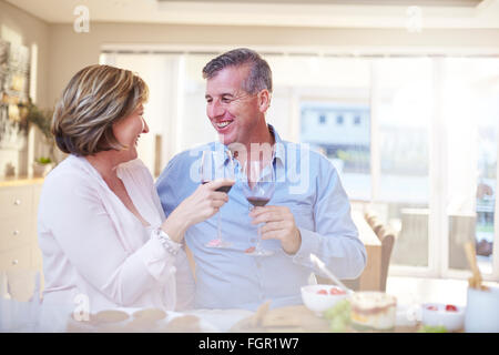 Smiling couple toasting red wine glasses in kitchen Stock Photo