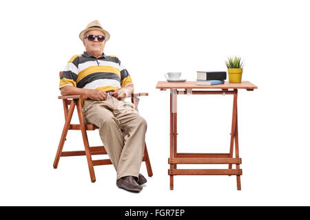 Cheerful senior gentleman sitting at a wooden table and looking at the camera isolated on white background Stock Photo