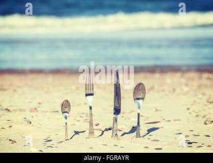 Retro toned cutlery stuck in sand on the beach, shallow depth of field. Stock Photo