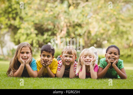 Smiling classmates lying in a row in grass Stock Photo