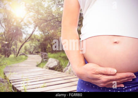 Composite image of pregnant woman holding baby shoes over bump Stock Photo