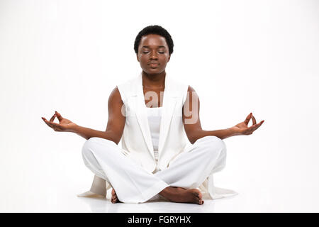 Pacified pretty african american young woman sitting and  meditating in lotus pose over white background Stock Photo