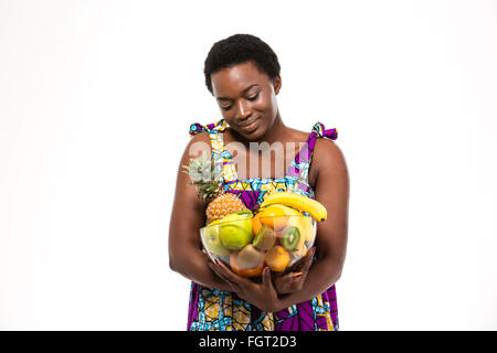 Cute lovely african american young woman in colorful sundress holding glass bowl with different fruits over white background Stock Photo