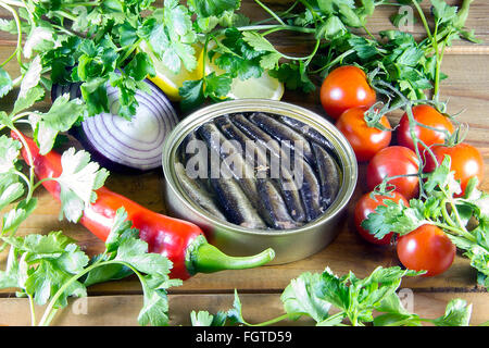 A can of sprats and vegetables scattered on a wooden table Stock Photo