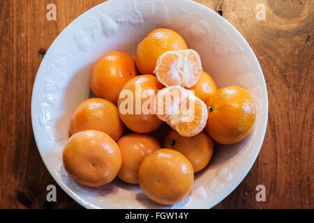 Mandarin oranges, Citrus reticulata, with one peeled, in a white bowl. Shot from above. Stock Photo