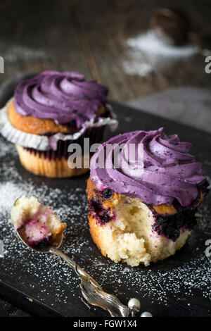 Delicious blueberry cupcakes with purple blueberry cream on wooden cutting board. Close up. Homemade sweet baking Stock Photo
