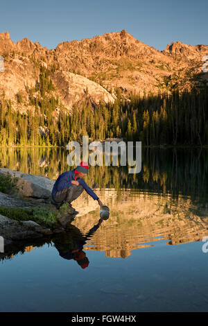 ID00339-00...IDAHO - Backpacker dipping a pan into Alpine Lake in the early morning in the Sawtooth Wilderness Area. Stock Photo