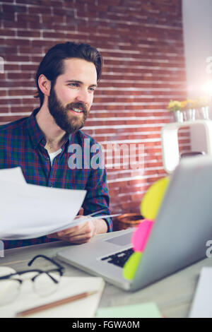 Smiling creative businessman with documents using laptop Stock Photo