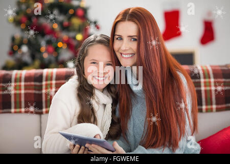 Composite image of festive mother and daughter using tablet on the couch Stock Photo