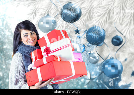 Composite image of smiling brunette holding pile of gifts Stock Photo