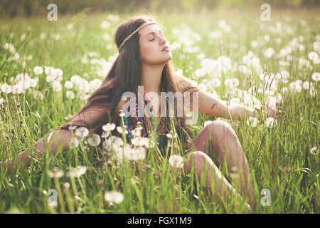 Beautiful hippie woman enjoying sun light in flowered meadow. Harmony with nature Stock Photo