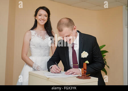 stylish groom looking at his beautiful bride signing wedding register