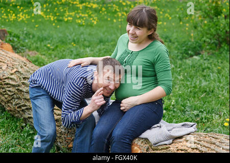 Man is listening to a pregnant wife's belly on wooden deck Stock Photo
