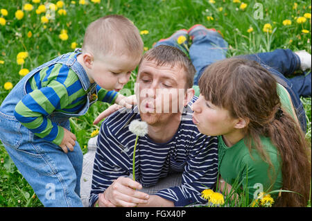 mom dad and son together blowing on a dandelion in a meadow Stock Photo