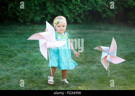 happy smiling little girl standing on meadow and holding toy white pinwheel windmill Stock Photo