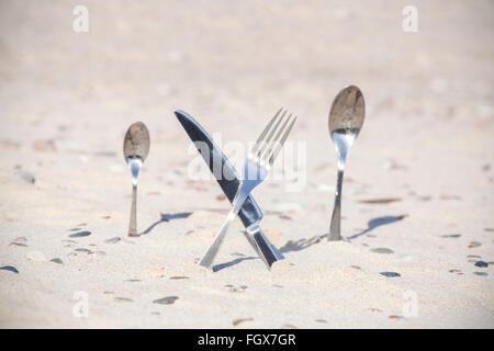 Cutlery stuck in sand on the beach, shallow depth of field. Stock Photo