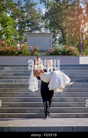 groom carries his bride in his arms on the stairs Stock Photo