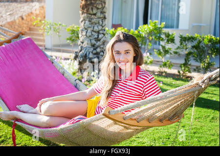 Happy relaxed young woman lying on hammock in casual summer dress Stock Photo