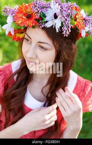 beautiful woman with a wreath sitting on the grass in a meadow Stock Photo