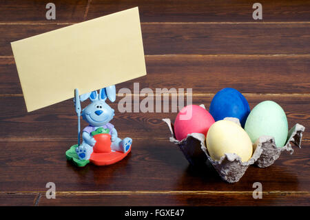 Colorful easter eggs in stand with bunny with greeting card over wooden background Stock Photo