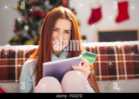 Composite image of festive redhead shopping online with tablet Stock Photo