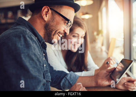 Close up portrait of happy young couple using a digital tablet together at a coffee shop. Young man and woman looking at touch s