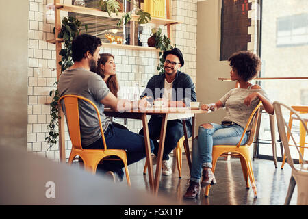 Young people sitting at a cafe table. Group of friends talking in a coffee shop. Stock Photo