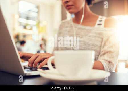 Woman sitting at a coffee shop working on laptop, with focus on hands typing on keyboard. Stock Photo