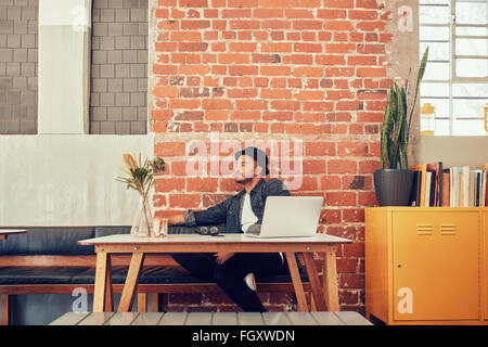 Portrait of young man sitting alone at a cafe with laptop on table. Caucasian man waiting for someone at coffee shop. Stock Photo