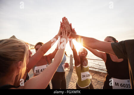Athletic team with their hands stacked together celebrating success. Marathon runners giving high five. Stock Photo