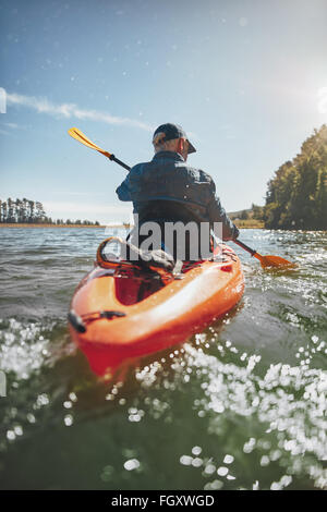 Rear view image of a mature man canoeing in a lake. Senior man paddling a kayak on summer day. Stock Photo