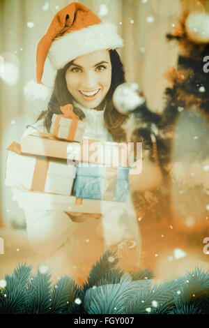 Composite image of festive brunette holding pile of gifts near a christmas tree Stock Photo