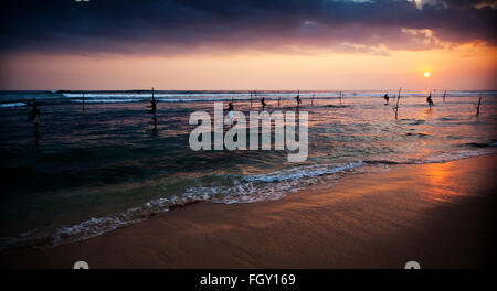 Silhouettes of the traditional stilt fishermen at sunset near Galle in Sri Lanka Stock Photo