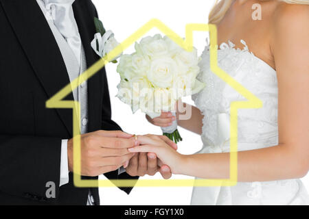 Composite image of young bridegroom putting on the wedding ring on his wifes finger Stock Photo