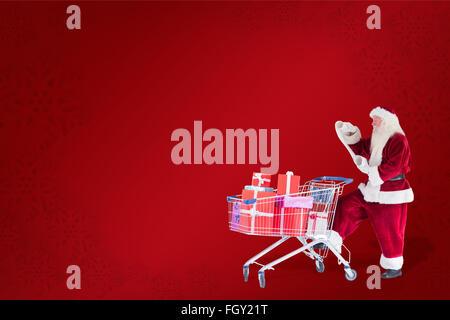 Composite image of santa pushes a shopping cart while reading Stock Photo