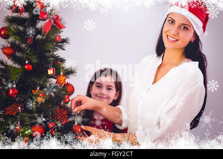 Composite image of mother and daughter hanging christmas decorations on tree Stock Photo