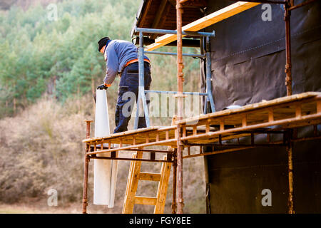 Construction worker on scaffold thermally insulating house, blac Stock Photo