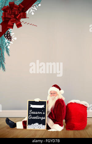 Composite image of santa sits leaned on his bag with a board Stock Photo