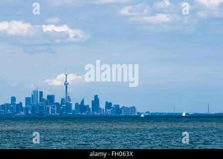 Toronto city skyline tinted in blue, from across rippled water against cloudy sky. Some boats sailing on lake in front of city. Stock Photo