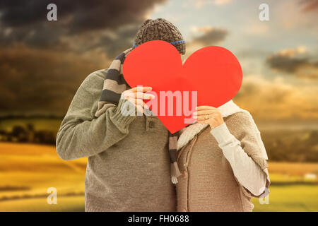 Composite image of happy mature couple in winter clothes holding red heart Stock Photo