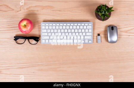 Overhead view of basic oak office desktop consisting of computer keyboard, mouse, thumb drive, reading glasses, baby plant Stock Photo