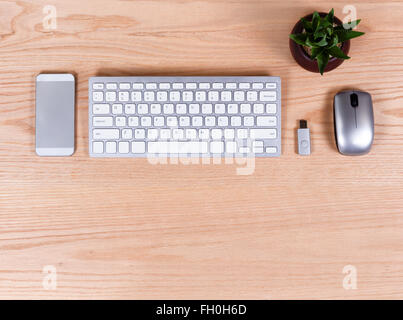 Overhead view of basic office desktop consisting of computer keyboard, mouse, thumb drive, cell phone on oak surface. Stock Photo