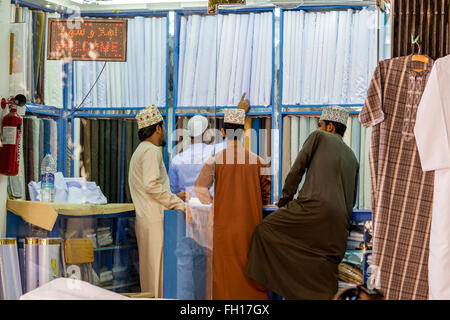 Young Omani Men Choosing Fabrics At A Shop In The Nizwa Souk, Nizwa, Ad Dakhiliyah Region, Oman Stock Photo