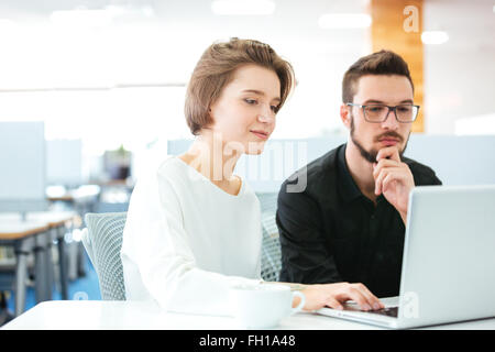 Concentrated young man and woman sitting and discussing new project using laptop in office Stock Photo