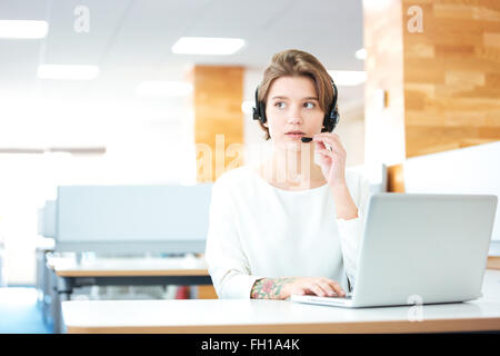 Beautiful young woman in headset sitting and working in call center in office