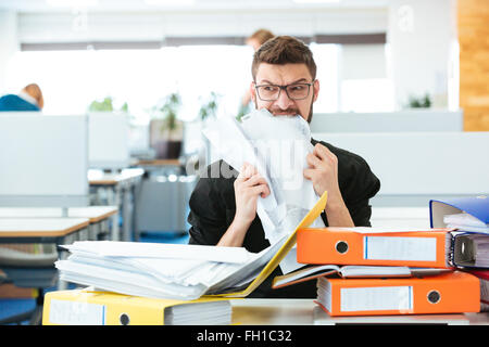 Young businessman biting paper in office Stock Photo