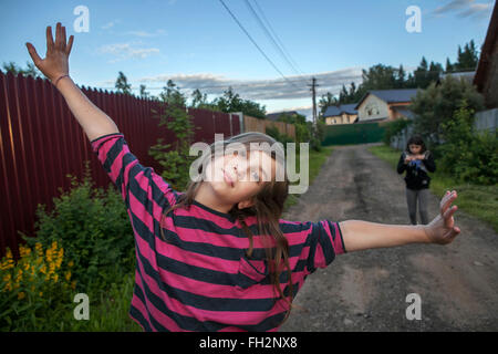 smiling teenage girl in a red striped shirt standing on the street between the houses, her arms up to the sky. Stock Photo